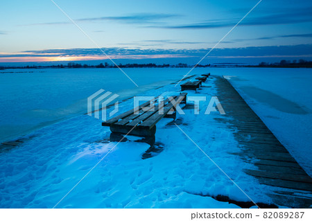 Wooden pier with benches and a snow-covered lake Wooden pier with benches and a snow-covered lake 82089287