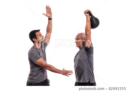 An elderly European man, with a personal trainer, trains, lifting weights, on a white background. 82091555
