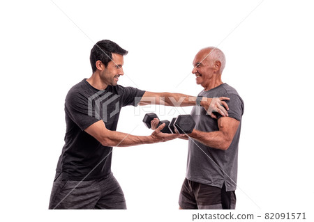 An elderly European man, with a personal trainer, trains, lifting weights, on a white background. 82091571