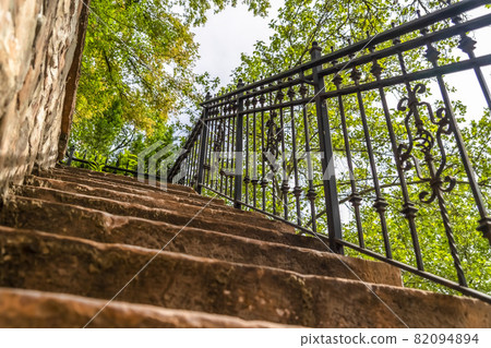 Close up of staircase with stone treads and metal railing against leaves and sky 82094894