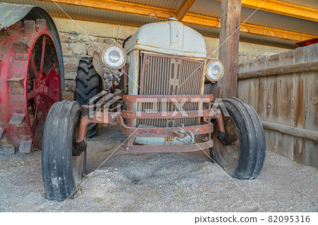 Front of an old and vintage tractor against stone wall and roof of a farm barn 82095316