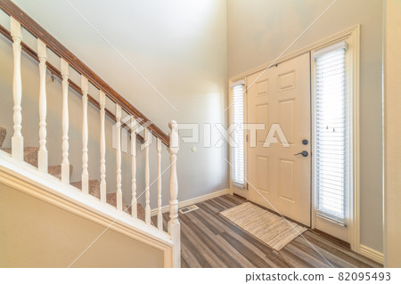 Home interior with stairs in front of the white front door flanked by sidelights 82095493