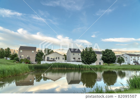 Scenic suburban landscape with homes and cloudy sky reflected on a shiny pond Scenic suburban landscape with homes and cloudy sky reflected on a shiny pond 82095507