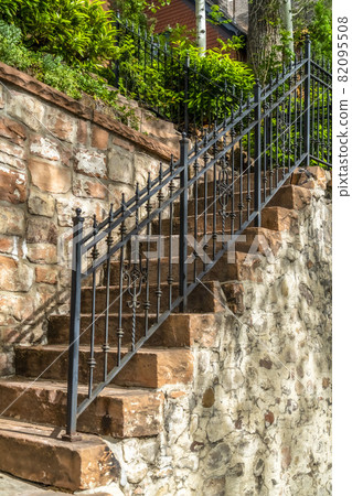 Outdoor staircase with stone steps and black metal railing against a fence 82095508