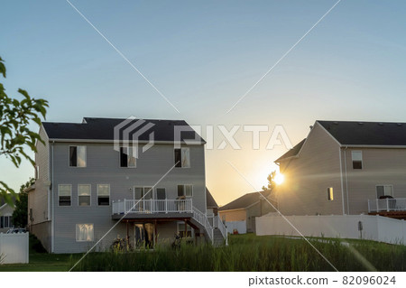 Home with balconies outdoor stairs and fence against sun and sky at sunset 82096024