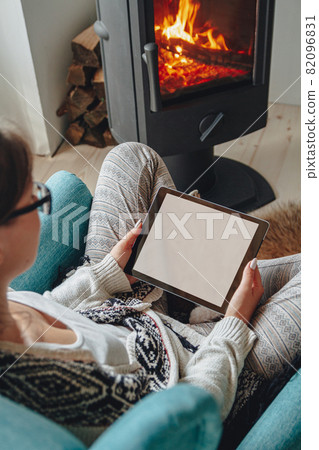 woman by the fireplace, sitting in a cozy armchair, with a warm 82096831
