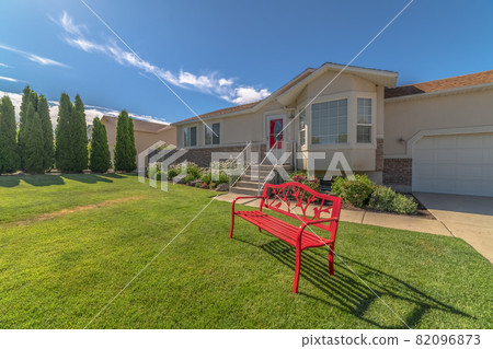 Red metal bench on the front yard of a home against blue sky on a sunny day Red metal bench on the front yard of a home against blue sky on a sunny day 82096873