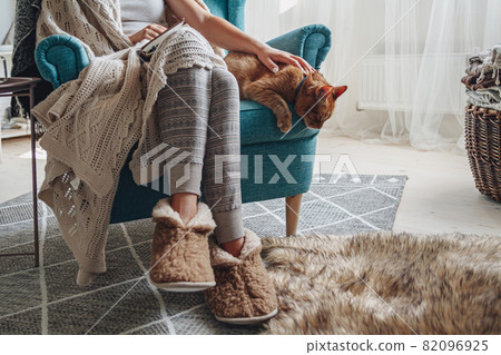 Young woman sitting in a cozy armchair, with a warm blanket, wit 82096925
