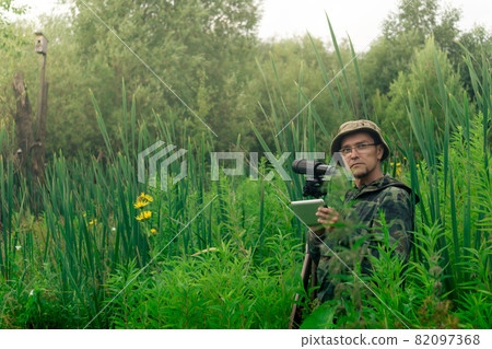 ornithologist with a spotting scope and notepad among the tall grass in the valley ornithologist with a spotting scope and notepad among the tall grass in the valley 82097368