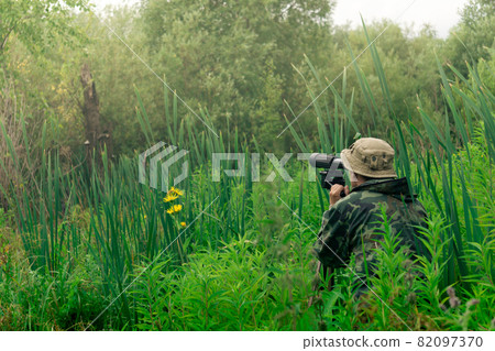 male explorer makes observations in the wild with a spotting scope standing among the tall grass male explorer makes observations in the wild with a spotting scope standing among the tall grass 82097370