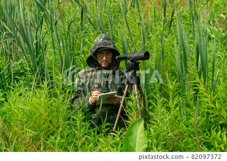 ornithologist records the results of the observations while standing among the tall grass in the wetland 82097372