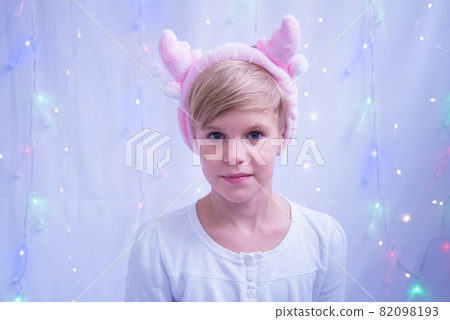 Portrait of a very beautiful child with blond hair. Girl with Christmas reindeer horns. A light smile and an attentive look. Bright blue eyes. The child is preparing for the New Year and Christmas Portrait of a very beautiful child with blond hair. Girl with Christmas reindeer horns. A light smile and an attentive look. Bright blue eyes. The child is preparing for the New Year and Christmas 82098193