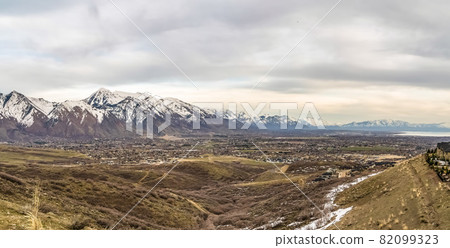 Panoramic view of snow capped mountain towering over the lake and valley Panoramic view of snow capped mountain towering over the lake and valley 82099323