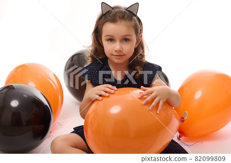 4 y.o adorable pretty little girl in witch costume plays with black and orange balloons isolated on white background. Concept of a happy child having fun at Traditional seasonal event, Halloween party 4 y.o adorable pretty little girl in witch costume plays with black and orange balloons isolated on white background. Concept of a happy child having fun at Traditional seasonal event, Halloween party 82099809