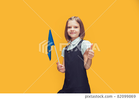 Smiling schoolgirl with small flag of European Union showing thumb-up. Education in Europe concept Smiling schoolgirl with small flag of European Union showing thumb-up. Education in Europe concept 82099869