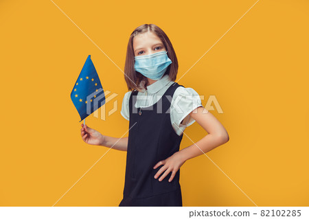 Little cute schoolgirl in protective mask holding a flag of the European union. Safety concept  82102285