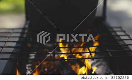 the pot stands on a burning fire, cooking on a camping trip, cooking in a fire pit in nature, outdoor activities, lighting a fire, delicious travel recipes, adventure season, slow motion 82102286