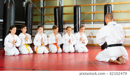 Coach in kimono tanding and greeting his students before lesson in gym Coach in kimono tanding and greeting his students before lesson in gym 82102479