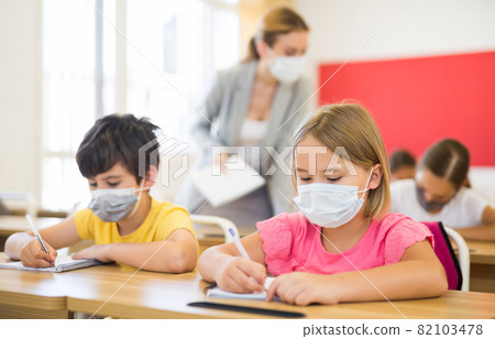 Schoolkids in face masks sitting at desks 82103478