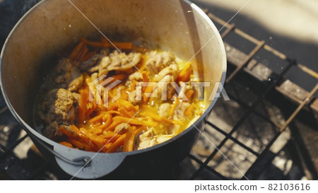 Meat with carrots and ground black pepper is boiled in a pot in nature, the pan is steaming and bubbling with protein broth, tourist recreation, food on the fire, a happy family dinner 82103616