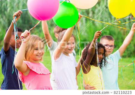 Happy tweens with balloons on green meadow in summer park 82110223