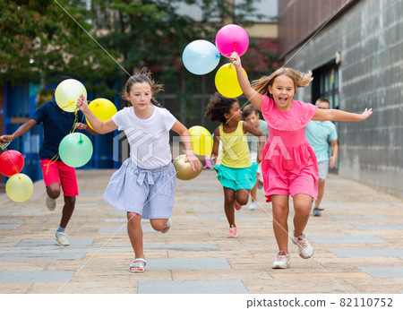 Happy tweens wth colorful balloons chasing each other on city street 82110752