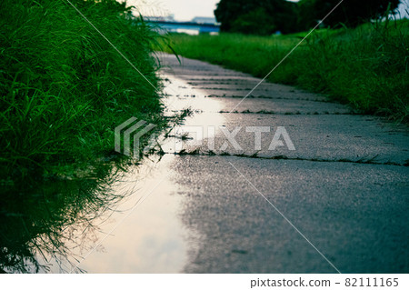 The blue sky is reflected in the puddle on the side of the road 82111165