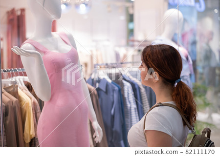 Caucasian woman looking at a shop window and dreaming about a dress. Caucasian woman looking at a shop window and dreaming about a dress. 82111170