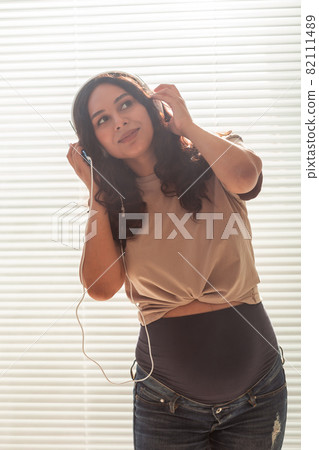 Pregnant woman listen to music in headphones at home and dances Pregnant woman listen to music in headphones at home and dances 82111489