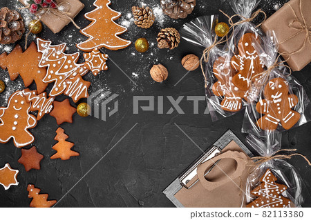 A Christmas gingerbread cookie in the shape of a Christmas tree in a cellophane packing on the background of a dark table. Christmas gift concept. 82113380
