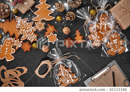 A Christmas gingerbread cookie in the shape of a Christmas tree in a cellophane packing on the background of a dark table. Christmas gift concept. A Christmas gingerbread cookie in the shape of a Christmas tree in a cellophane packing on the background of a dark table. Christmas gift concept. 82113386