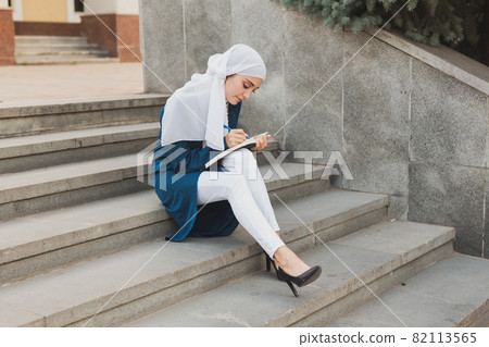 Arab female student sitting on stairs in downtown. 82113565