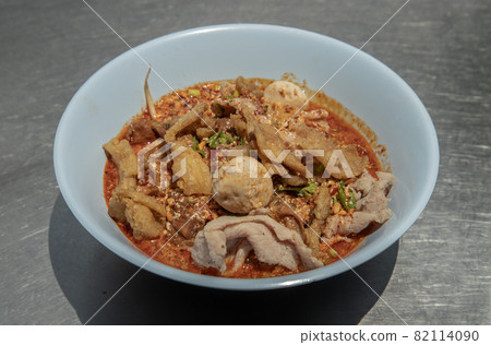 Egg noodles in Thai spicy soup with braised pork, pork balls and fatty pork rinds in white bowl. 82114090