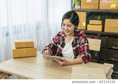 Asian woman startup small business at home office. Online seller entrepreneur young asian woman use tablet checking online order. Woman using tablet check stock goods supply delivery package shipping Asian woman startup small business at home office. Online seller entrepreneur young asian woman use tablet checking online order. Woman using tablet check stock goods supply delivery package shipping 82114110
