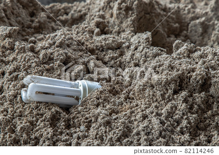 The remains of burnt energy-saving lamp are left on the beach sand. Hazardous and toxic electronic waste. The remains of burnt energy-saving lamp are left on the beach sand. Hazardous and toxic electronic waste. 82114246