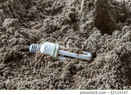 The remains of burnt energy-saving lamp are left on the beach sand. Hazardous and toxic electronic waste. The remains of burnt energy-saving lamp are left on the beach sand. Hazardous and toxic electronic waste. 82114247