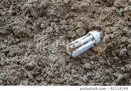 The remains of burnt energy-saving lamp are left on the beach sand. Hazardous and toxic electronic waste. The remains of burnt energy-saving lamp are left on the beach sand. Hazardous and toxic electronic waste. 82114249