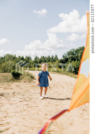 A little girl is flying a kite on a field road outside the city. Childhood, joy, care A little girl is flying a kite on a field road outside the city. Childhood, joy, care 82115977