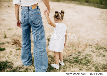 Mom and her little daughter are walking, holding hands, spending time together Mom and her little daughter are walking, holding hands, spending time together 82115980