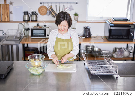 一個穿著圍裙的年輕女人用刀切洋蔥 82116760