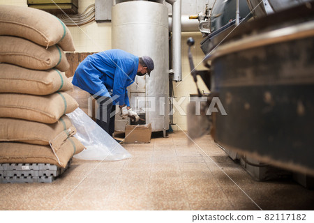 Man in uniform setting up roasting machine 82117182