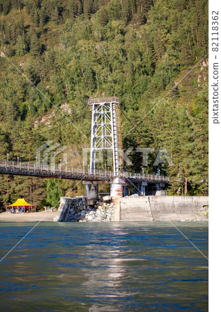 A suspension bridge over a wide river in the mountains. Safe crossing of the bridge from one bank to the other. A suspension bridge over a wide river in the mountains. Safe crossing of the bridge from one bank to the other. 82118362