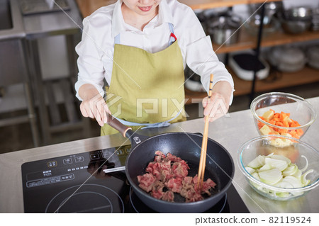 A young woman in an apron frying beef in the kitchen 82119524