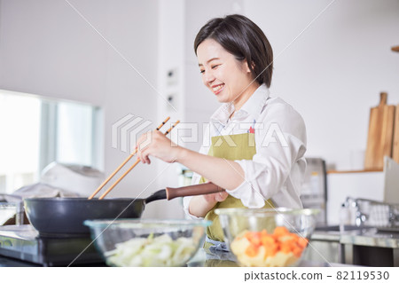 A young woman in an apron cooking in the kitchen 82119530