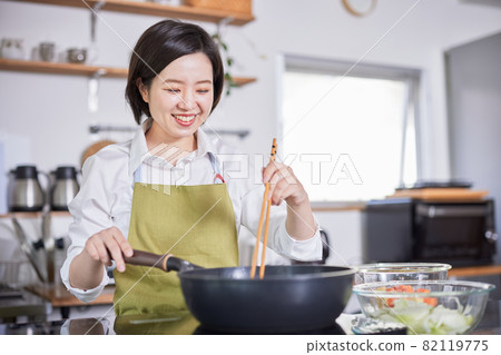 A young woman in an apron cooking in the kitchen 82119775