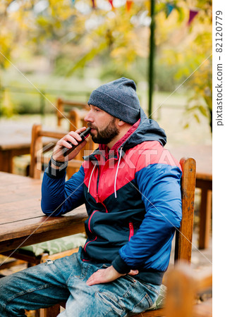 A young man using a mobile phone is sitting outdoors in a cafe or restaurant on an autumn day A young man using a mobile phone is sitting outdoors in a cafe or restaurant on an autumn day 82120779