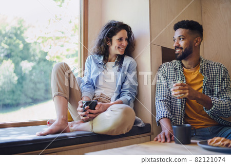 Happy couple sitting, resting and drinking coffee indoors in a tree house, weekend away and digital detox concept. Happy couple sitting, resting and drinking coffee indoors in a tree house, weekend away and digital detox concept. 82121074