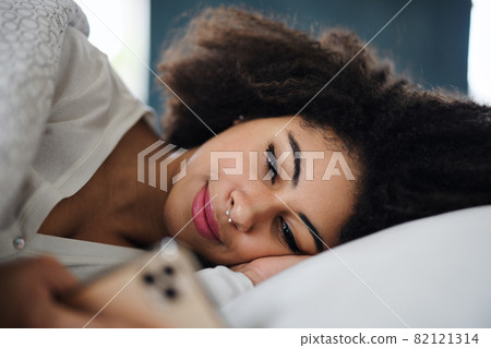 Front view portrait of young woman indoors on bed, using smartphone. Front view portrait of young woman indoors on bed, using smartphone. 82121314