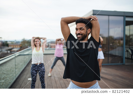 Group of young people doing exercise outdoors on terrace, sport and healthy lifestyle concept. 82121402