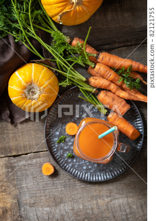 Fresh natural mixed juice, healthy food concept. Glass jar of fresh carrot juice with fresh carrots and pumpkin on a wooden rustic table. Top view flat lay background. 82121755